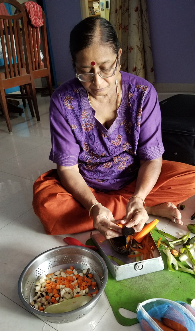 Amma uses a traditional boti knife to cut vegetables while sitting on the floor. 